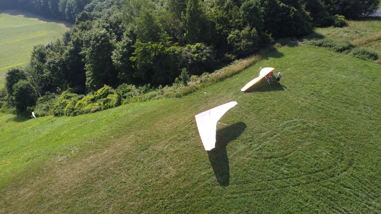 A hang glider launching over a green Western New York ridge